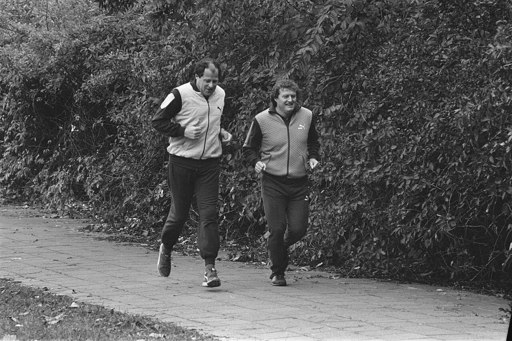 Training Feijenoord ivm Uefa-Cup-wedstrijd tegen Borussia Mönchen-Gladbach; trainer Rinus Beek (l) en assistent Wim Jansen tijdens een looptraining. Foto: fotograaf onbekend / Anefo, Nationaal Archief (CC0).