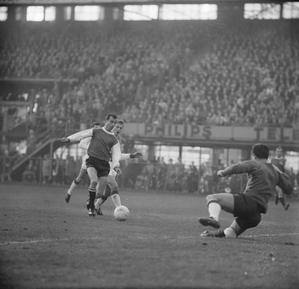 Feijenoord-Ajax 9-4 (29 november 1964). Coen Moulijn in duel met Günther de Haan, met Ajax-keeper Bertus Hogerman. Foto: Jac. de Nijs / Anefo, Nationaal Archief (CC0).