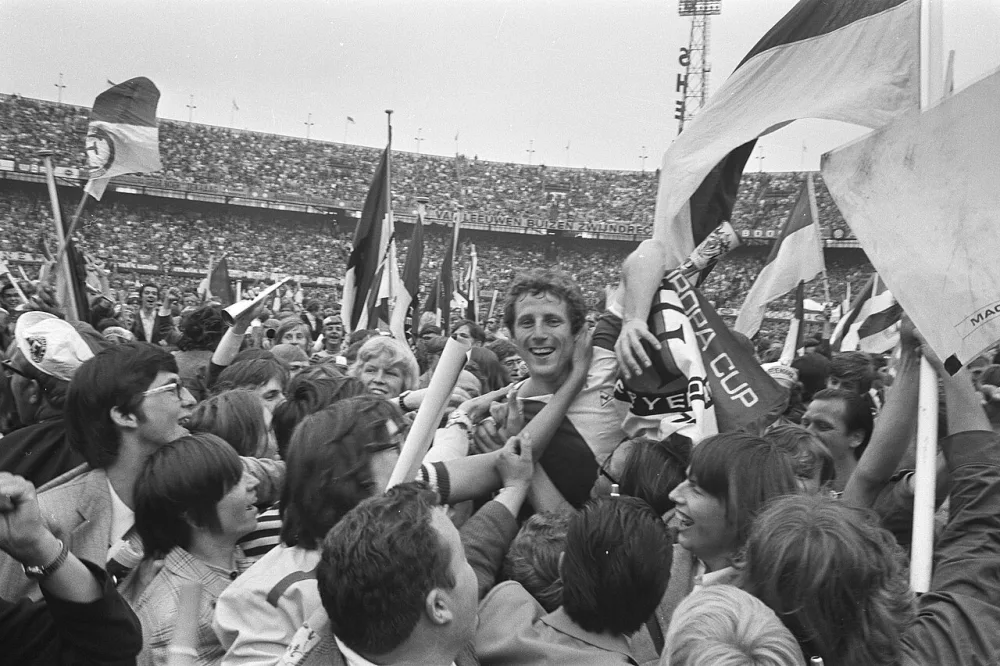 Door de overwinning is Feyenoord kampioen; Feyenoord-speler Schneider wordt op de schouders genomen door supporters. Foto: fotograaf onbekend / Anefo, Nationaal Archief (CC0).